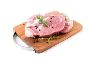 Stücke von Schweinefleisch Fleisch mit Rosmarin und Thymian Blätter auf Holz Teller isoliert auf Weiß foto