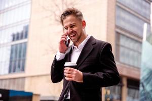 Kerl im ein passen spricht auf das Telefon lacht und Spaziergänge mit Kaffee im seine Hände Nahansicht foto