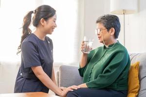 asiatisch jung Frau Betreuer, Pfleger unterstützen Alten, alt geduldig beim heim, Trinken Wasser nach nehmen Medizin, heilen oder Behandlung Krankheit von Oma nach Ruhestand, Hilfe Unterstützung. foto