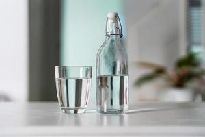 ein Glas von sauber Trinken Wasser und ein Wasser Flasche auf ein Weiß hölzern Tabelle foto
