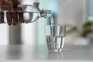 gießen das Wasser von das Wasser Flasche in das Glas foto