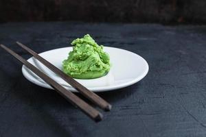 Wasabi auf weißem Teller mit Essstäbchenpaar auf schwarzem Tischhintergrund foto