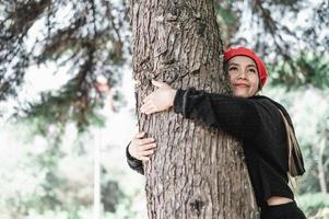 zufrieden jung Frau umarmen ein groß Baum mit ein glückselig Ausdruck mit Kopieren Raum foto
