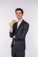 Porträt des jungen lächelnden hübschen Geschäftsmannes, der die Kreditkarte lokalisiert über weißem Hintergrund zeigt foto