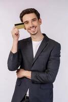 Porträt des jungen lächelnden hübschen Geschäftsmannes, der die Kreditkarte lokalisiert über weißem Hintergrund zeigt foto