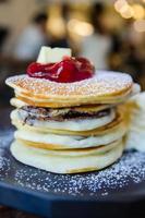 Stapel von Pfannkuchen mit Erdbeere auf oben auf schwarz Teller foto