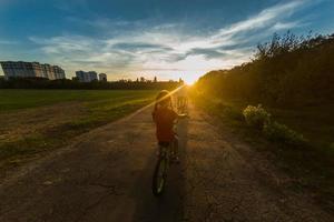 Familie von drei Menschen haben Reiten im ländlich Landschaft. Sohn, Mutter und Vater Reiten Fahrräder Über Sonnenuntergang Himmel Hintergrund. Familie Biker haben Spaß auf Urlaube. foto