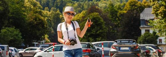 Frau zeigen ihr Neu Auto Schlüssel lächelnd glücklich posieren im das Parkplatz Menge draußen, draußen im Sommer- Tag foto