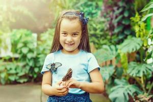 Lachen lockig Mädchen mit ein Schmetterling auf seine Hand. glücklich Kindheit Konzept. Hintergrund Tonen zum instagram Filter. foto