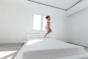 süß wenig Mädchen Springen auf Weiß Bett foto