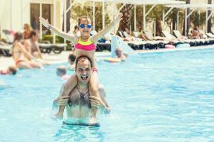 glücklich Familie, aktiv Vater mit wenig Kind, bezaubernd Kleinkind Mädchen, haben Spaß zusammen im draußen Schwimmen Schwimmbad im Wasserpark während Sommer- Meer Ferien im tropisch Resort foto