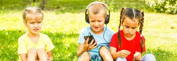 Unternehmen von drei Kinder im das Park sind Sitzung auf das Gras mit ein Telefon foto