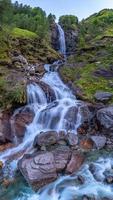 ein hoch Wasserfall umgeben durch hoch Gras und ein Wandern Weg foto