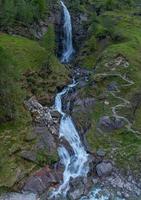 ein hoch Wasserfall umgeben durch hoch Gras und ein Wandern Weg foto