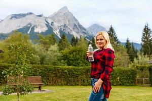 Alpen. ein Frau Trinken Wasser von ein Flasche und bewundern das Berg Landschaft. foto
