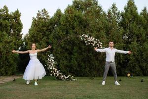 das zuerst tanzen von das Bräutigam und Braut im ein kurz Hochzeit Kleid auf ein Grün Wiese foto