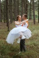 jung Paar Braut im ein Weiß kurz Kleid und Bräutigam im ein grau passen im ein Kiefer Wald foto