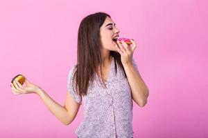 Schönheit Modell- Mädchen Essen bunt Donuts. komisch froh gestylt Frau wählen Süßigkeiten auf Rosa Hintergrund. Diät, Diät Konzept. Müll Essen, abnehmen, Gewicht Verlust foto