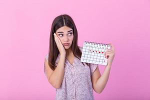 jung schön Frau halten Menstruation Kalender Über isoliert Hintergrund mit Überraschung Gesicht. jung Mädchen halten Menstruation Kalender mit verwirrt Gesicht, Angst und aufgeregt mit Angst Ausdruck foto