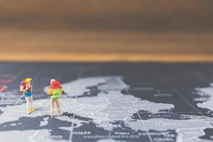 Miniatur-Rucksacktouristen, die auf einer Weltkarte, einem Tourismus- und Reisekonzept spazieren gehen foto