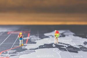 Miniatur-Rucksacktouristen, die auf einer Weltkarte, einem Tourismus- und einem Reisekonzept spazieren gehen foto