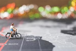 Miniaturreisender, der Fahrrad auf einer Weltkarte fährt, reist und das Weltkonzept erforscht foto