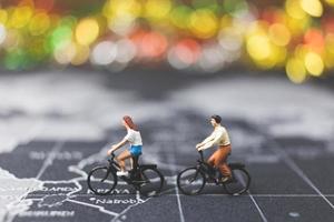 Miniaturreisende, die Fahrrad auf einer Weltkarte fahren, reisen und das Weltkonzept erkunden