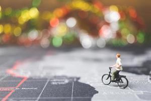 Miniaturreisender, der Fahrrad auf einer Weltkarte fährt, reist und das Weltkonzept erforscht foto