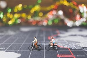Miniaturreisende, die Fahrrad auf einer Weltkarte fahren, reisen und das Weltkonzept erkunden