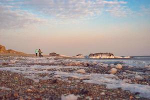 Leute, die entlang Glasstrand gegen einen bunten bewölkten Himmel in Wladiwostok, Russland gehen foto