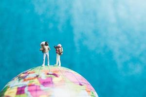 Miniaturreisende mit Rucksäcken, die auf einer Weltkugel stehen und zu einem Ziel gehen foto