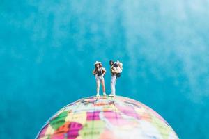 Miniaturreisende mit Rucksäcken, die auf einer Weltkugel stehen und zu einem Ziel gehen