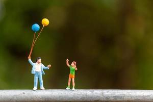 Miniaturfamilie, die bunte Luftballons hält, glückliches Familienkonzept