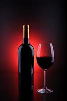 Weinflasche mit schwarzem Hintergrund und rotem Vollglas foto