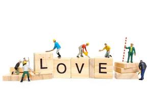 Miniaturarbeiter, die das Wort Liebe auf Holzklötzen mit einem weißen Hintergrund, Valentinstagskonzept bauen