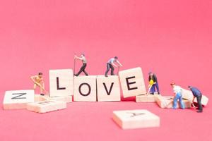 Miniaturarbeiter, die das Wort Liebe auf Holzklötzen mit einem rosa Hintergrund, Valentinstagskonzept bauen