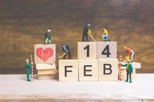 Miniaturarbeiter, die die Wörter und Daten für Valentinstag auf Holzklötzen mit hölzernem Hintergrund, Valentinstagkonzept bauen foto