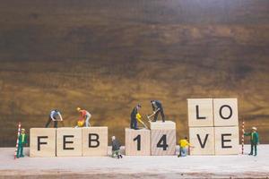 Miniaturarbeiter, die die Wörter und Daten für Valentinstag auf Holzklötzen mit hölzernem Hintergrund, Valentinstagkonzept bauen foto