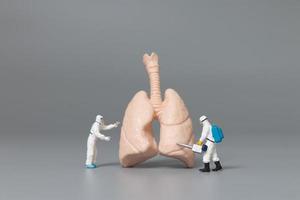 Miniaturärzte und Krankenschwestern, die das Konzept der menschlichen Lunge, des Virus und der mit Bakterien infizierten Menschen beobachten und diskutieren foto
