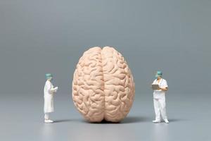 Miniaturarzt und Krankenschwester, die das menschliche Gehirn, die Wissenschaft und das medizinische Konzept beobachten und diskutieren foto