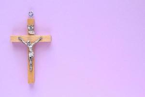 Kruzifix Christian hölzern Kreuz auf lila Hintergrund. katholisch Symbol. Flach, oben Sicht, legen aus, isoliert. beten zum Gott, Vertrauen im Jesus Christus und glauben Religion Konzept. Nahansicht