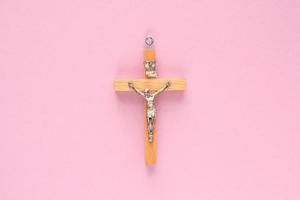 Kruzifix Christian hölzern Kreuz auf Rosa Hintergrund. katholisch Symbol. Flach, oben Sicht, legen aus, isoliert. beten zum Gott, Vertrauen im Jesus Christus und glauben Religion Konzept. Nahansicht foto