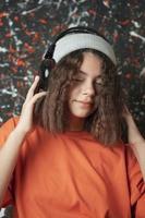 ein süß europäisch Teenager Mädchen im ein modisch Hut mit schön wellig Haar hört zu zu Musik- durch groß Kopfhörer foto