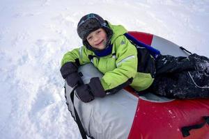 komisch kaukasisch Junge 5 Jahre alt Fahrten im Winter auf ein groß aufblasbar Käsekuchen foto