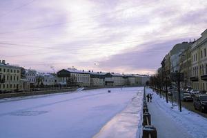 das Damm und das gefroren Stadt Fluss im Winter und Menschen gehen auf das Eis foto