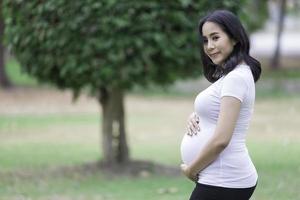 Porträt von asiatisch schön schwanger Frau beim das parken, thailand Leute, glücklich Frau Konzept, sie verwenden Hand berühren ihr Bauch, Mutter Tag Konzept foto