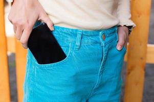 das Mädchen setzt das Telefon im das Vorderseite Tasche von ihr Blau Denim Hose foto