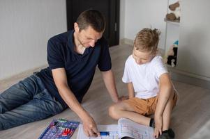 ein süß Junge im ein Weiß T-Shirt sammelt ein elektrisch Designer mit seine Papa im das Zimmer foto