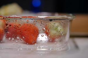 das Glas bedeckt mit Wasser Tröpfchen hält Erdbeeren foto