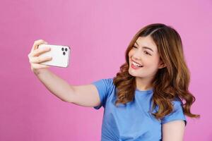 Porträt einer glücklich lächelnden jungen Frau, die ein lässiges T-Shirt-Selfie mit Smartphone trägt, das über rosafarbenem Hintergrund isoliert ist foto